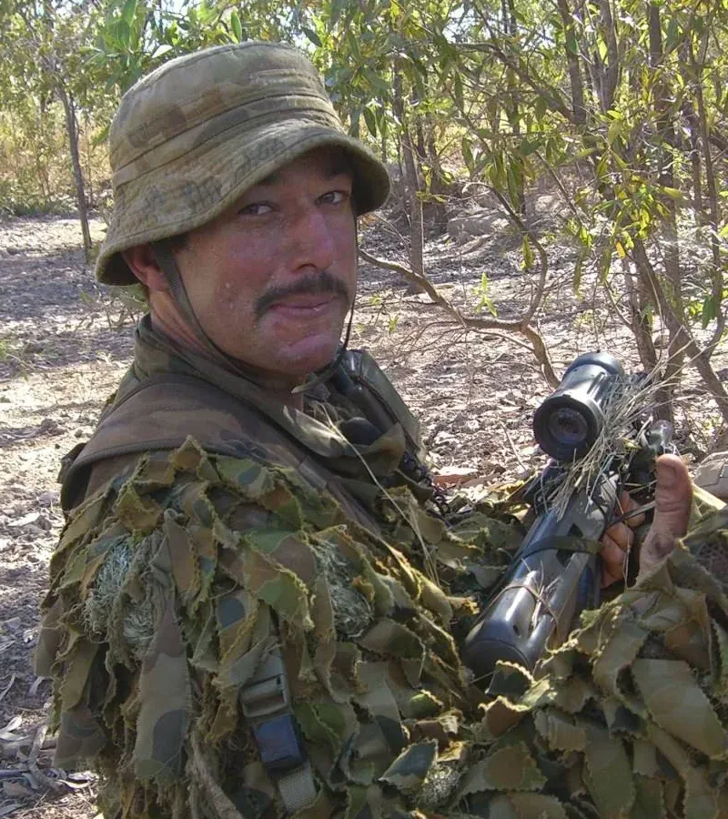 Robert Keegan in camouflage during RAAF field training, smiling and giving a thumbs-up